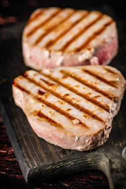 Delicious grilled tuna steak on a cutting board. On a rustic dark background. High quality photo