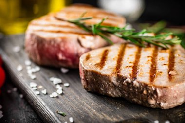 Grilled tuna on a cutting board with a sprig of rosemary. Against a dark background. High quality photo