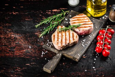 Grilled tuna steak on a cutting board with spices, tomatoes and rosemary. Against a dark background. High quality photo