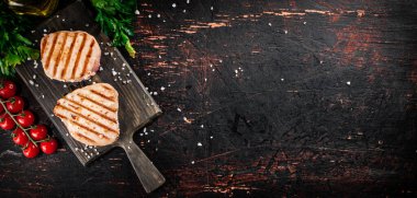 Grilled tuna on a cutting board with parsley and tomatoes. Against a dark background. High quality photo