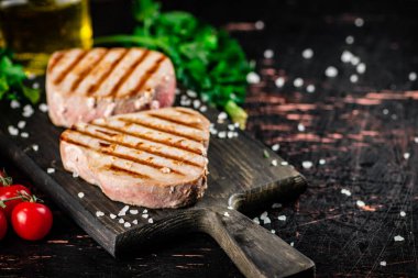 Grilled tuna on a cutting board with parsley and tomatoes. Against a dark background. High quality photo