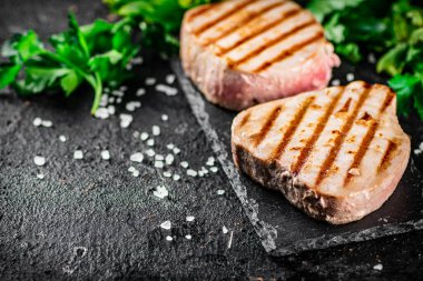 Grilled tuna on a stone board with parsley and salt. On a black background. High quality photo