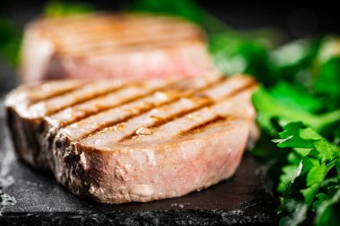 Grilled tuna on a stone board with parsley and salt. On a black background. High quality photo