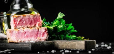Grilled tuna steak on a parsley cutting board. On a black background. High quality photo