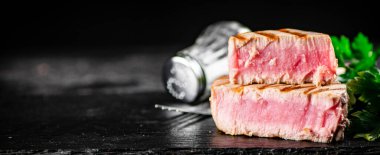 A piece of grilled tuna with parsley. On a black background. High quality photo