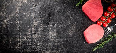 Fresh raw tuna steak with tomatoes and rosemary. On a black background. High quality photo