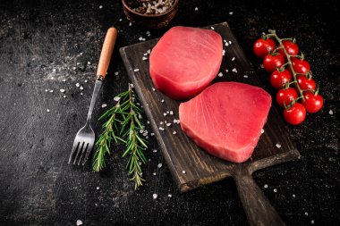 Fresh raw tuna on a cutting board with tomatoes, spices and rosemary. On a black background. High quality photo