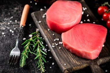Fresh raw tuna on a cutting board with tomatoes, spices and rosemary. On a black background. High quality photo