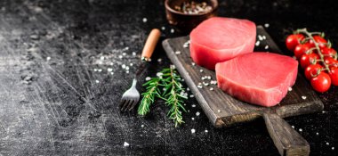 Fresh raw tuna on a cutting board with tomatoes, spices and rosemary. On a black background. High quality photo