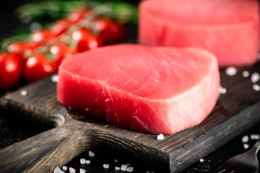 Fresh raw tuna on a cutting board with cherry tomatoes. Against a dark background. High quality photo