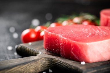 Fresh raw tuna on a cutting board with cherry tomatoes. Against a dark background. High quality photo