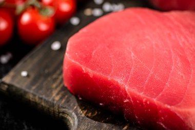 Fresh raw tuna on a cutting board with cherry tomatoes. Against a dark background. High quality photo