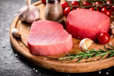 Raw tuna on a cutting board with garlic, tomatoes and spices. On a black background. High quality photo