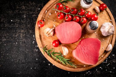 Raw tuna on a cutting board with garlic, tomatoes and spices. On a black background. High quality photo