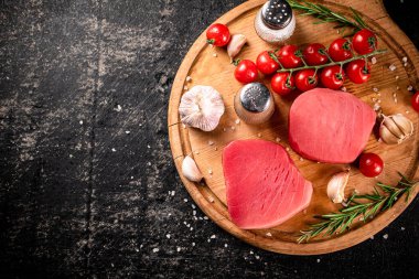 Raw tuna on a cutting board with garlic, tomatoes and spices. On a black background. High quality photo