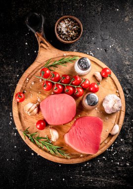 Raw tuna on a cutting board with garlic, tomatoes and spices. On a black background. High quality photo