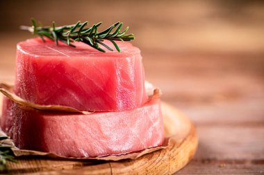 A steak of raw tuna on a cutting board with a sprig of rosemary. On a wooden background. High quality photo