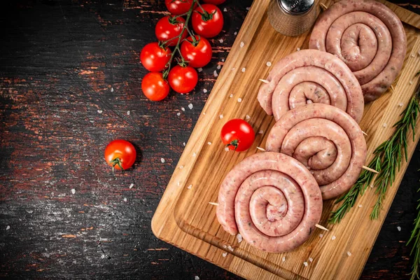 Raw sausages on a cutting board with a sprig of rosemary and tomatoes. On a rustic dark background. High quality photo