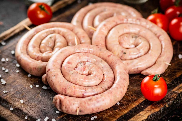 Raw sausages on a wooden cutting board with tomatoes. On a rustic background. High quality photo