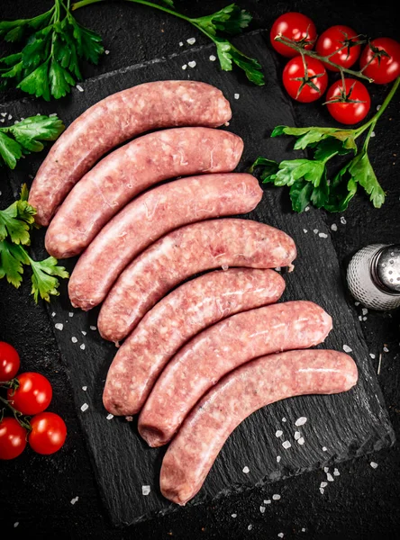 Raw sausages on a stone board with spices, tomatoes and herbs. On a black background. High quality photo