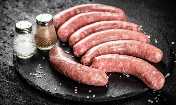 Raw sausages on a stone board with spices. On a black background. High quality photo