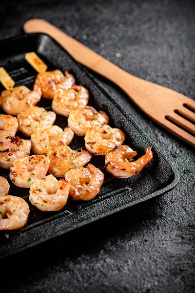 Shrimp on skewers are grilled in a grill pan. On a black background. High quality photo