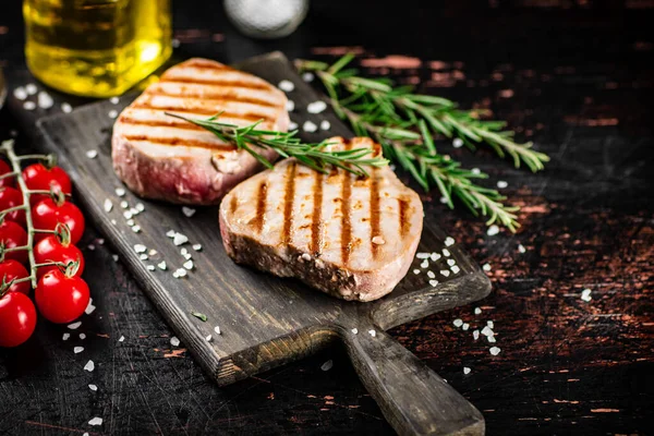 stock image Grilled tuna steak on a cutting board with spices, tomatoes and rosemary. Against a dark background. High quality photo