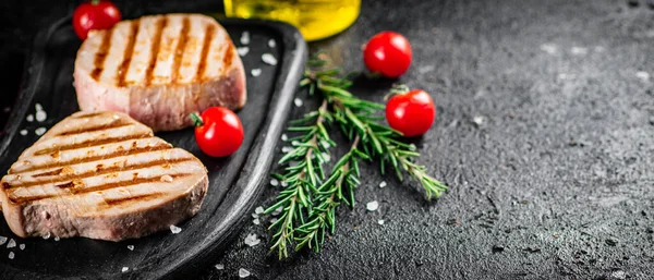 Grilled tuna on a tray with tomatoes and rosemary. On a black background. High quality photo