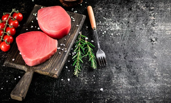 Fresh raw tuna on a cutting board with tomatoes, spices and rosemary. On a black background. High quality photo