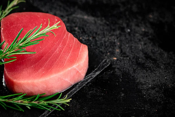 Raw tuna on a stone board with rosemary. On a black background. High quality photo