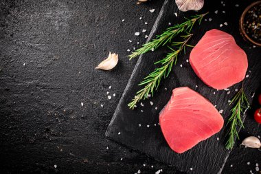 Raw tuna on a stone board with rosemary and garlic. On a black background. High quality photo