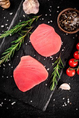 Raw tuna steak on a stone board with rosemary, spices and tomatoes. On a black background. High quality photo