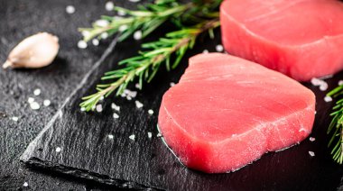 Raw tuna on a stone board with rosemary and garlic. On a black background. High quality photo
