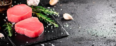 Raw tuna on a stone board with rosemary and garlic. On a black background. High quality photo