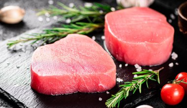 Raw tuna on a stone board with rosemary and garlic. On a black background. High quality photo