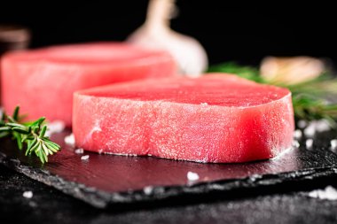 Raw tuna on a stone board with rosemary and garlic. On a black background. High quality photo