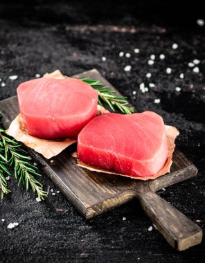 Raw tuna steaks on a rosemary cutting board. On a black background. High quality photo