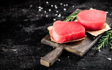 Raw tuna steaks on a rosemary cutting board. On a black background. High quality photo