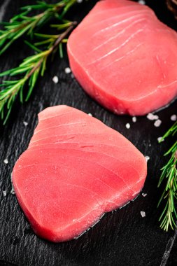 Raw tuna on a stone board with rosemary. On a black background. High quality photo