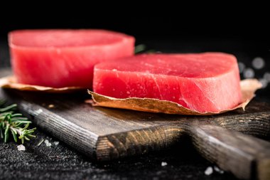 Raw tuna steaks on a rosemary cutting board. On a black background. High quality photo