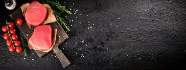 Raw tuna on a cutting board with tomatoes and rosemary. On a black background. High quality photo
