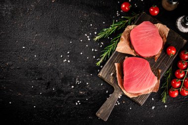 Raw tuna on a cutting board with tomatoes and rosemary. On a black background. High quality photo