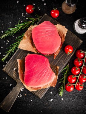 Raw tuna on a cutting board with tomatoes and rosemary. On a black background. High quality photo