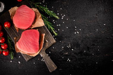 Raw tuna on a cutting board with tomatoes and rosemary. On a black background. High quality photo
