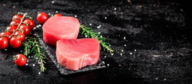 Raw tuna on a stone board with rosemary and tomatoes. On a black background. High quality photo