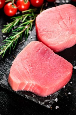 Raw tuna on a stone board with rosemary and tomatoes. On a black background. High quality photo