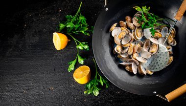 Vongole in a saucepan with lemon slices and parsley. On a black background. High quality photo