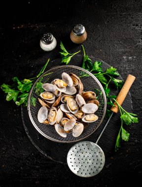 Fresh vongole in a colander on a stone board with parsley. On a black background. High quality photo