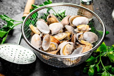 Fresh vongole in a colander on a stone board with parsley. On a black background. High quality photo
