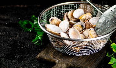 Vongole in a colander on a cutting board with parsley. On a black background. High quality photo